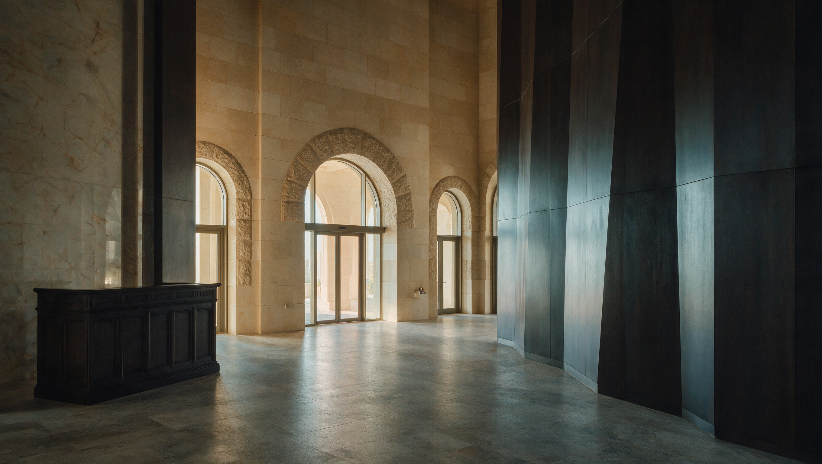 A Gulf hotel lobby at early morning in stone and dark timber, with a discreet commercial scent unit near the entrance