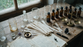 A perfumer's workbench from above: beakers, amber vials, blotter strips and a brass balance in cool north light